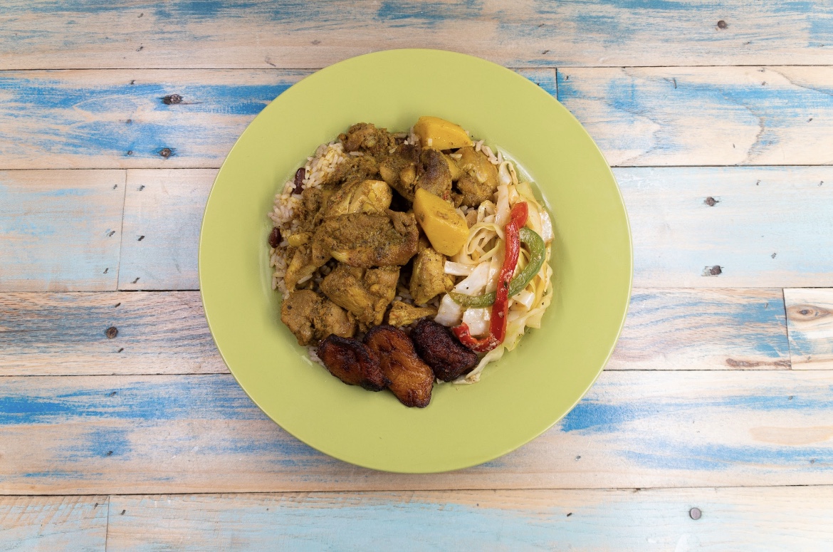 Top view of curry chicken with rice and peas, cabbage and plantains